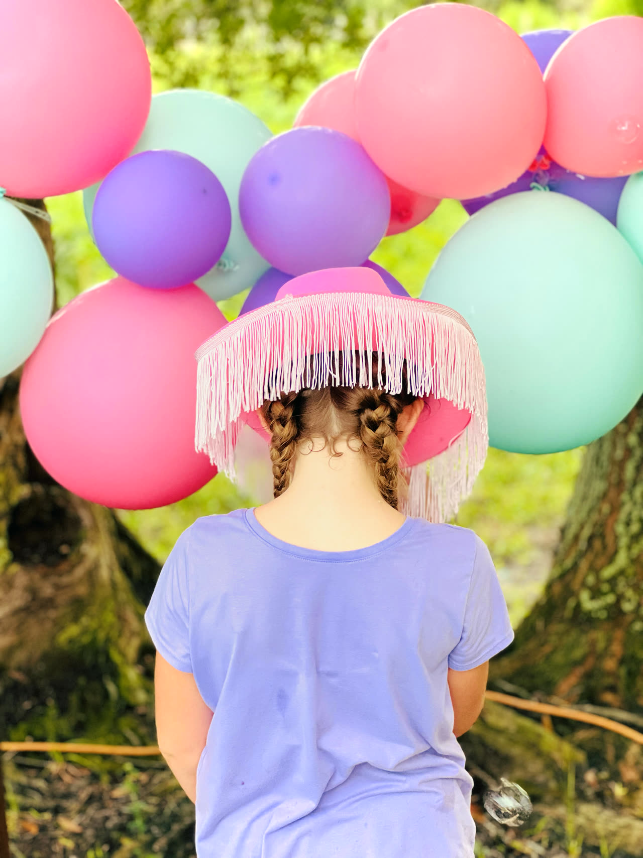 A child in a pink fringed cowgirl hat standing beneath a pastel balloon arch at a Once Upon a Pony party